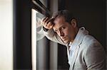 Thoughtful businessman leaning on window at office