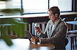 Concentrated business man using digital tablet and mobile phone in café