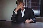 Tensed businessman sitting in office with hand on temples