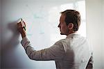 Rear-view of a businessman writing on white board at office