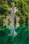 Rock cliff and trees reflected in emerald green lake water at the Plitvice Lakes National Park in Croatia