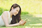 Portrait of young Japanese woman laying on grass with smartphone
