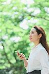 Young Japanese woman with smartphone surrounded by green in a city park