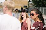 Three male and female friends laughing in city skatepark