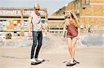 Young female and male skateboarding friends skateboarding in skatepark