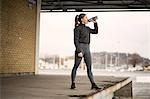 Female runner drinking bottled water on warehouse platform