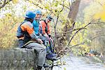 Male and female kayakers sitting on river bank wall laughing, River Dee, Llangollen, North Wales