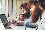 Male adult hipster twins working on laptop in office