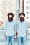 Portrait of identical male hipster twins standing on apartment roof terrace