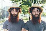 Portrait of identical male hipster twins wearing straw hats on sidewalk