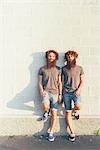 Portrait of identical adult male twins with red hair and beards against white wall