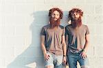 Portrait of identical adult male twins with red hair and beards against wall