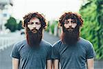 Portrait of identical adult male twins with red hair and beards on sidewalk