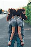 Portrait of identical adult male twins with red hair and beards back to back on sidewalk