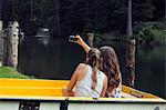 Two young female friends taking smartphone selfie in rowing boat, Sattelbergalm, Tirol, Austria