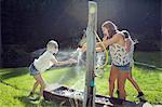 Three adult female friends play fighting sprinkling water hose in garden