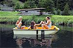 Three adult female friends having fun in rowing boat on lake, Sattelbergalm, Tirol, Austria