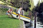 Three adult female friends launching rowing boat into lake, Sattelbergalm, Tirol, Austria