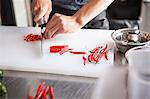 Cropped view of man slicing red chilli peppers