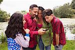 Family standing outdoors, looking at smartphone, smiling