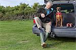 Man and dog sitting in car boot removing wellington boots