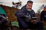 Hiker using digital tablet by tent, Keimiotunturi, Lapland, Finland