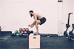 Young male cross trainer jumping on box in gym