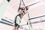 Low angle view of young male cross trainer training on exercise rings in gym