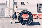 Young male cross trainer pushing large tyre outside gym