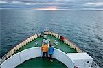 Tourists standing on the deck of a ship and admiring the sunrise.