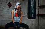Tough young woman sitting by boxing bag in the shed.