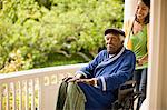 Smiling woman pushes a senior man in a wheelchair along a porch.