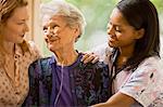 Senior woman with a ozygen nose hose (cannula) smiles as she is supported by a young woman and a female nurse.