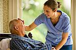 Female nurse leans over to place a hand on the forehead of a senior man lying in a bed.