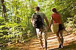 Rear view of couple holding hands while hiking in the forest.