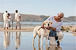 Mature woman kneeling next to a dog on a beach at low tide.