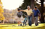 Smiling senior man having fun walking with his two grandsons through a park while wheeling a bicycle.