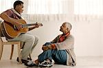 Smiling senior woman listening to her husband play an acoustic guitar.