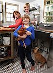 Mother and daughters in kitchen preparing folder, younger daughter holding pet chicken