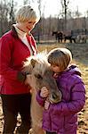Portrait of mother and daughter outdoors, standing with pony