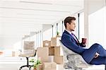 Side view of young businessman having coffee on chair in new office