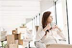 Thoughtful young businesswoman having coffee on chair in new office