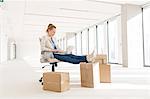 Full length of young businesswoman using laptop with feet up on cardboard box in new office