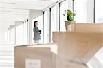 Distant image of businessman looking through window with cardboard boxes in foreground