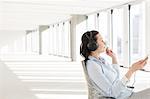 Side view of mid adult businesswoman listening music through headphones in empty office