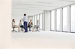 Mature businessman having discussion with colleagues sitting on chair in new office