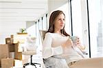 Thoughtful young businesswoman holding coffee cup in new office