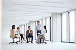 Mature businessman discussing with colleagues sitting on chair in new office