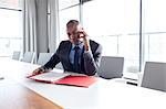 Young businessman holding file while talking on phone at conference table