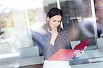 Young businesswoman with hand on chin reading file in office